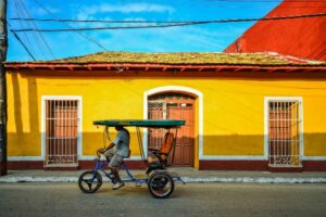 Fietstaxi Cuba bij geel gekleurd huis