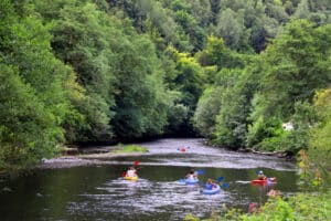 Gezinnen kanoën op een rivier in België tijdens een glampingvakantie met Vodatent, omringd door groene heuvels